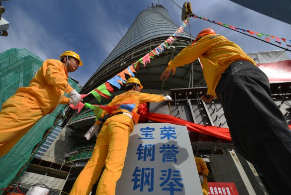 Construction workers watch as the final steel beam is hoisted to be put in place in a ceremony for the topping out of the Shanghai Tower 580x388 Worlds second tallest building, designed by United States firm Gensler, tops out in China